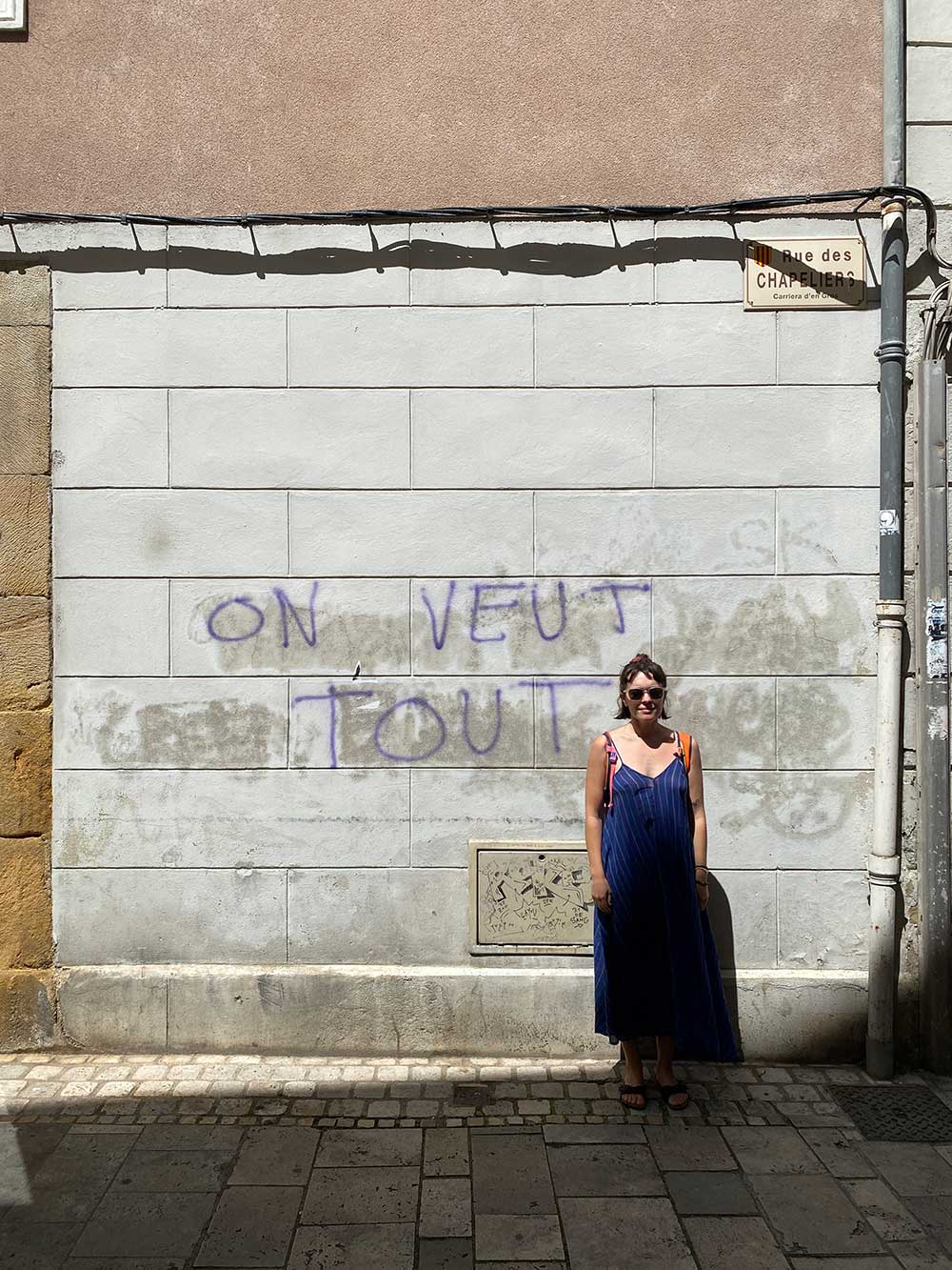 Woman standing beneath the words On veut tout painted on a wall.